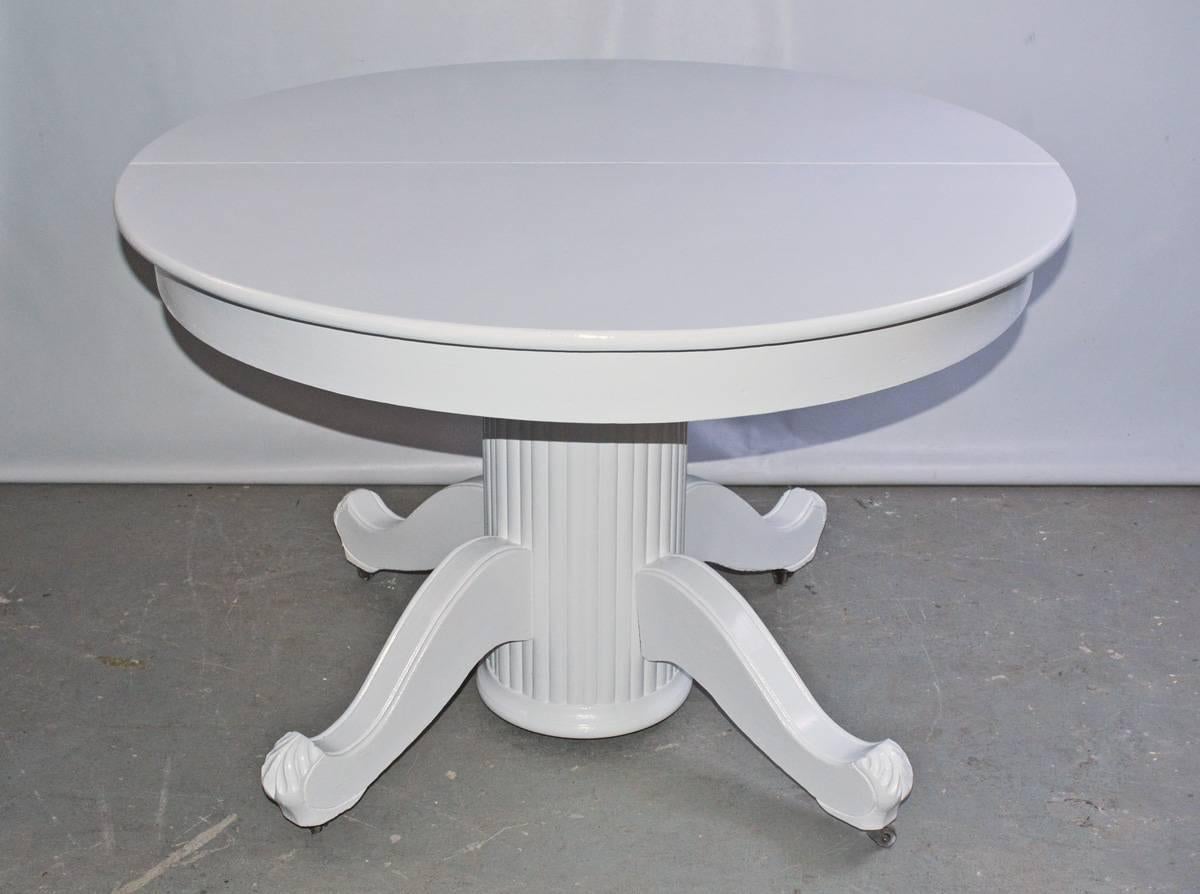 The Victorian round dining, breakfast or center table (library or hall) has a fluted pedestal leg with four splayed feet and attached casters. The table is painted glossy white. 