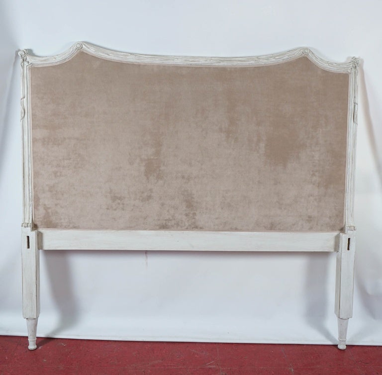 Neoclassical in design and upholstered in plush beige velvet, the white glazed frame of the headboard has hand-carved 