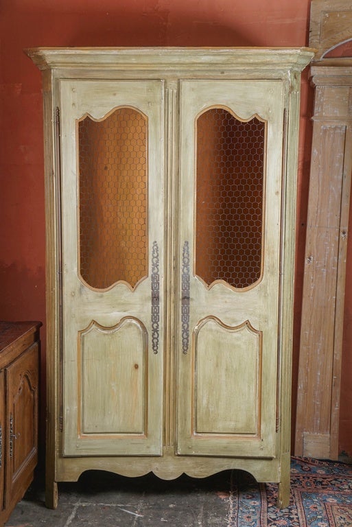 Constructed with a great sense of style, proportion and taste, this French Provincial style armoire in the Louis XV style with rubbed sage green paint, terracotta trim inside and out. The design includes fluted center supports and chicken wire