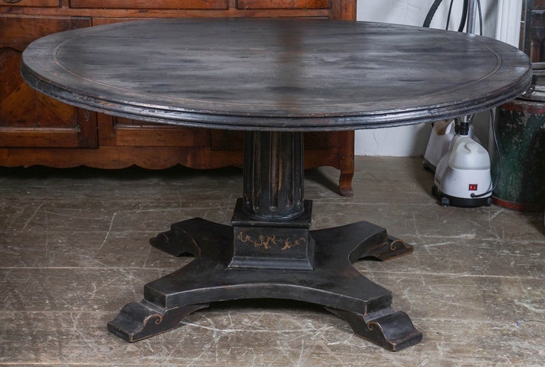 This European dining table is painted black with gilt designs, including center cartouche of a pair of lions and flowers and a border of flowers and leaves. The columned base has gilt leaves and flowers, as well as four splayed feet. Seats up to