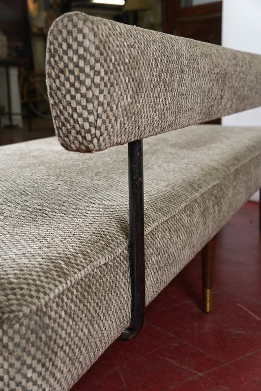 A Classic mid-20th century design, the seat of this sofa or daybed sits on six tapered wood legs with brass tips. The two back cushions rest against an upholstered bar that can be removed and the sofa can be turned into a bed. The upholstered fabric