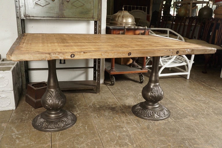 The top is made of rustic French industrial factory wood pellet with eight planks secured at each end by u-shaped iron bars, as well as by long bolts from side to side.  The base are a pair of pedestals made of cast iron decorated with acanthus