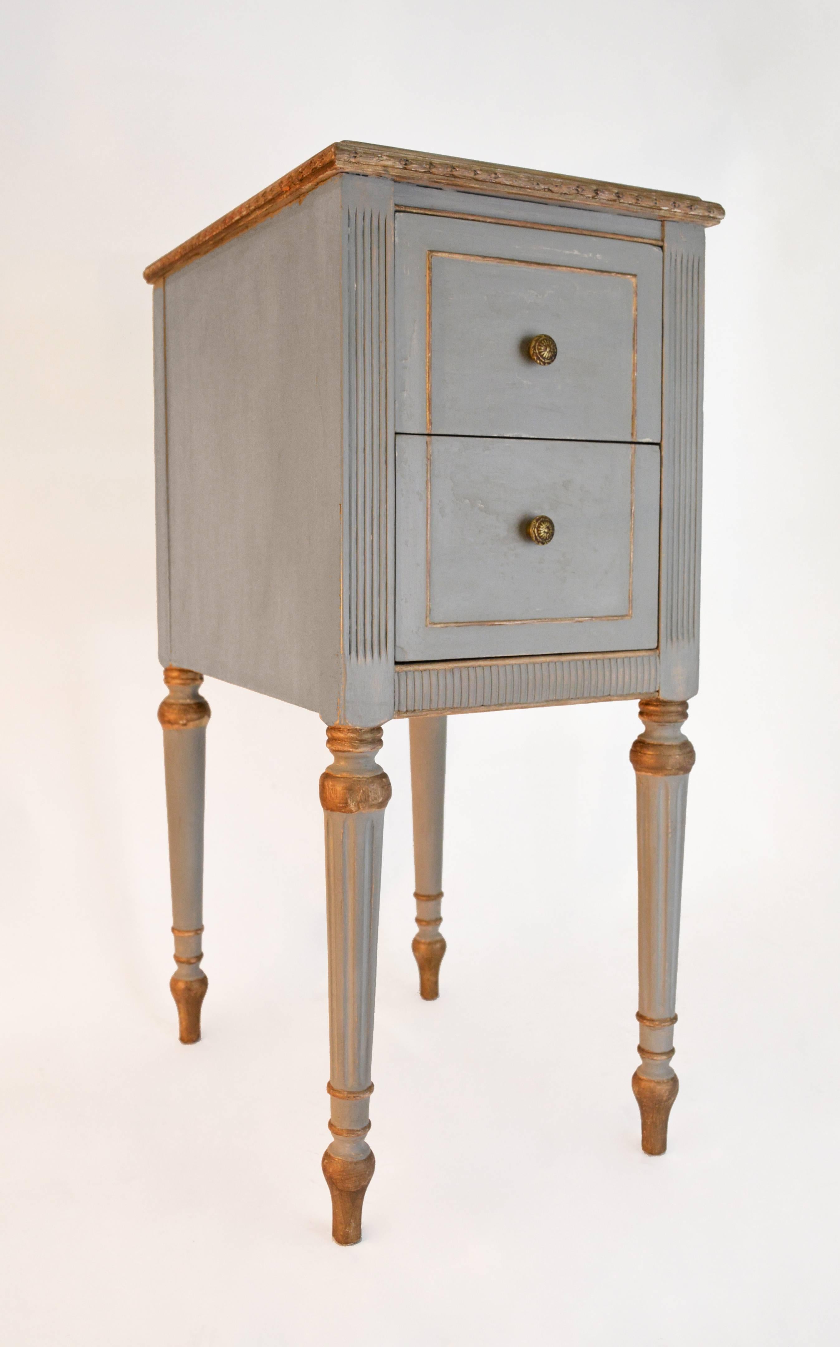 Gustavian Neoclassical style painted night stand with fluted panels surrounding three sides, pair of dovetailed drawers with brass pulls, as well as fluted legs.  Painted a light gray and trimmed in gilt.  Can also work with Louis XVI style decor.