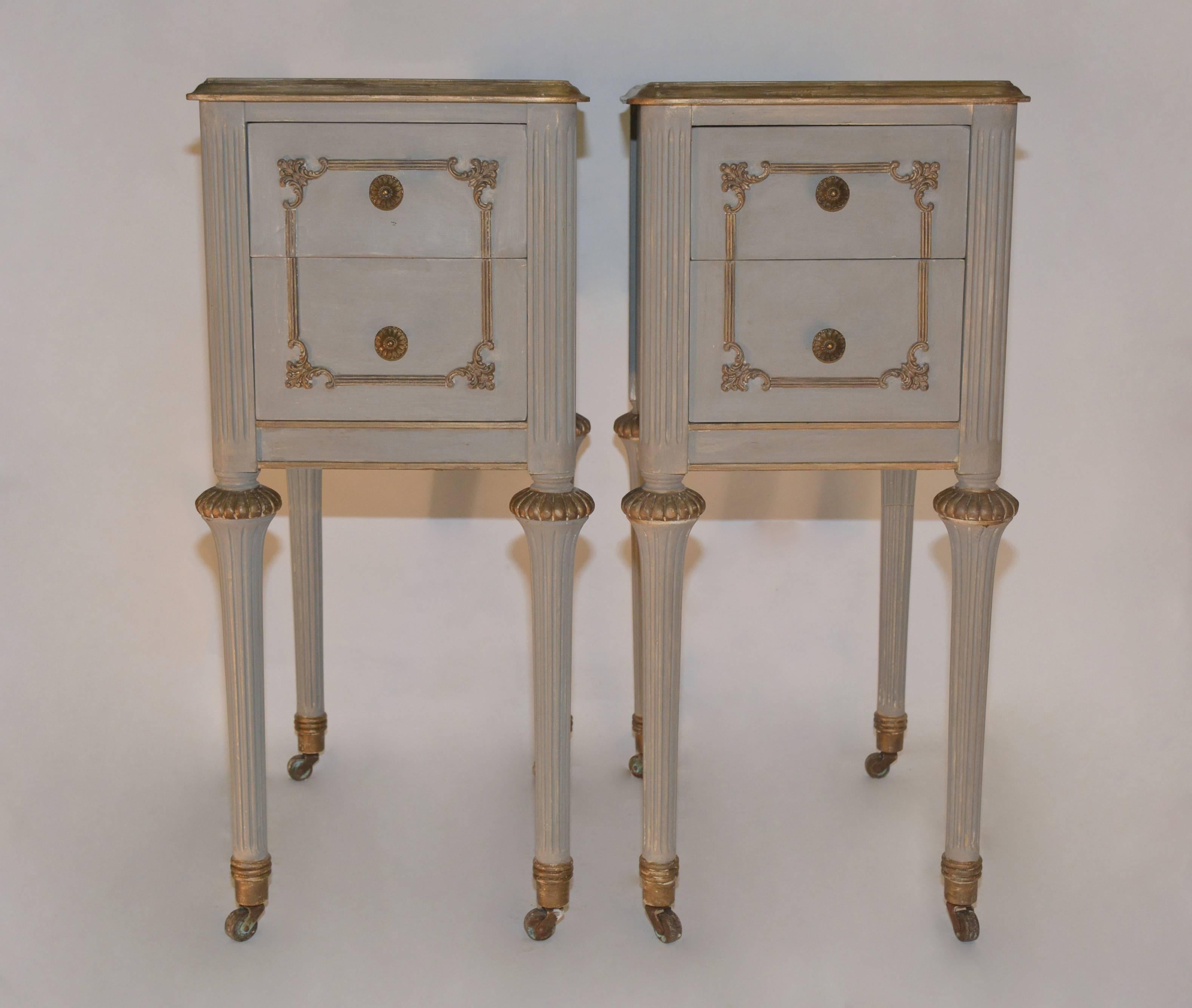 Pair of Louis XVI French style bedside tables with two decorative dovetail drawers, brass knobs, fluted legs, casters and fluted rounded corners. Both are painted grey with gilt trim. Will work well as night tabled in Gustavian Style setting.