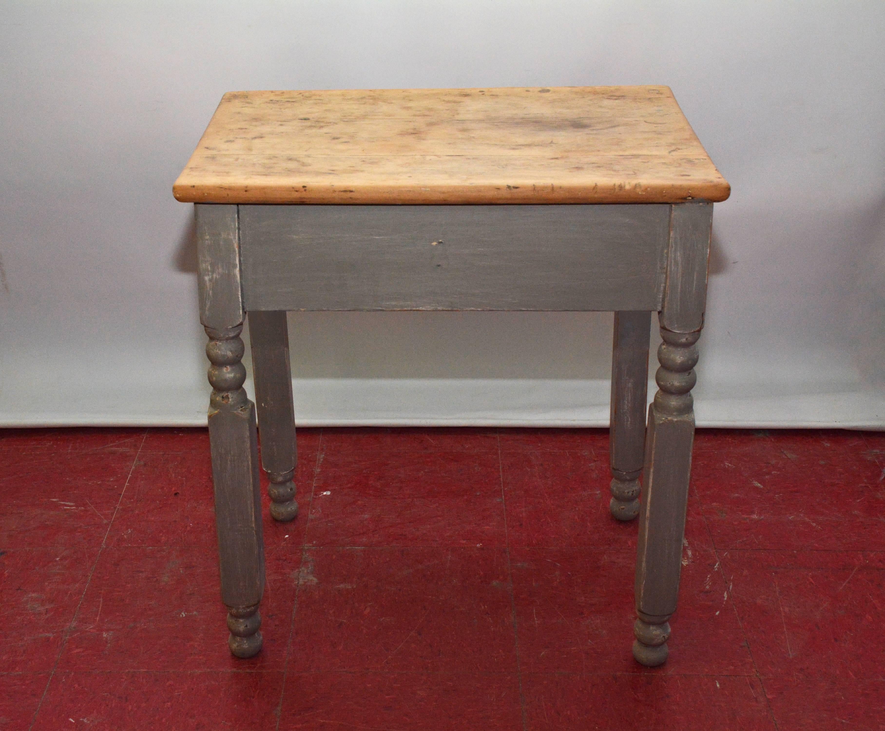 The rustic pine table or nightstand has a base with rubbed gray paint, partially turned legs and a single drawer. The top is natural pinewood.