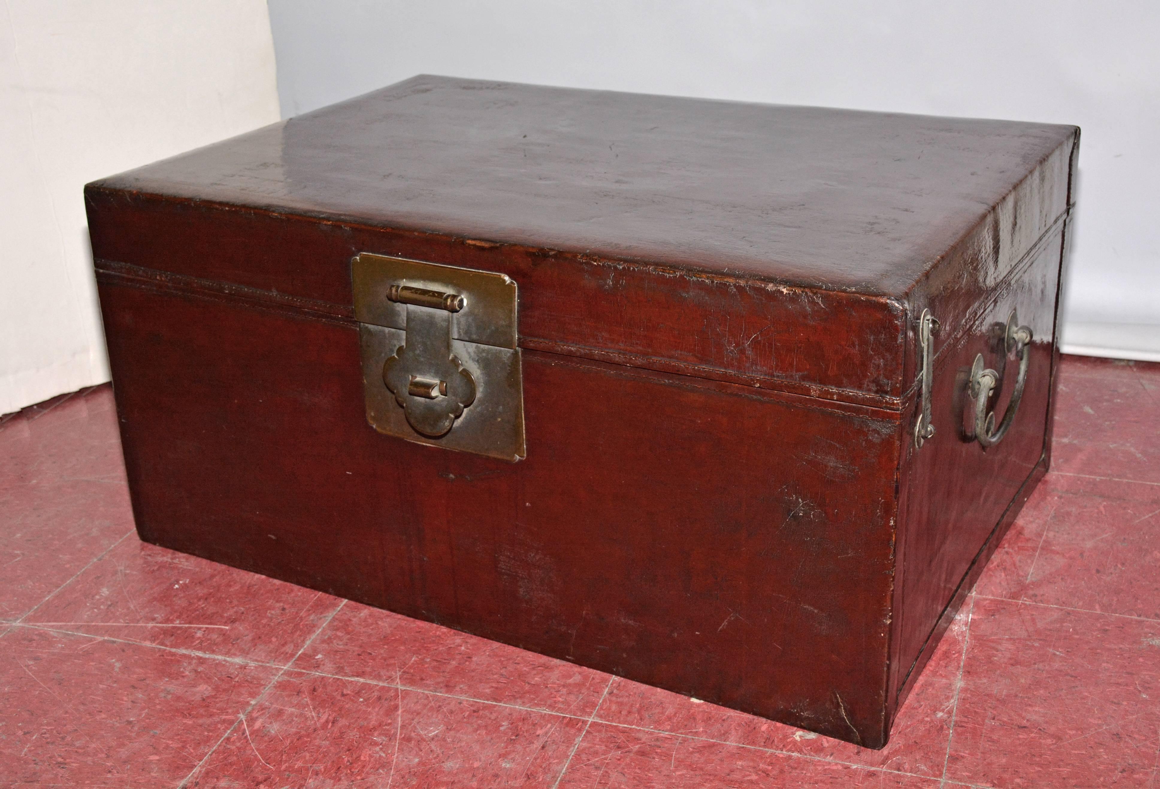 The chest has dark reddish brown lacquered wood on the outside and the inside is lined with tan imitation leather material.  There are three brass latches, one large one in front and a smaller one on each side next to iron handles.  The sides are