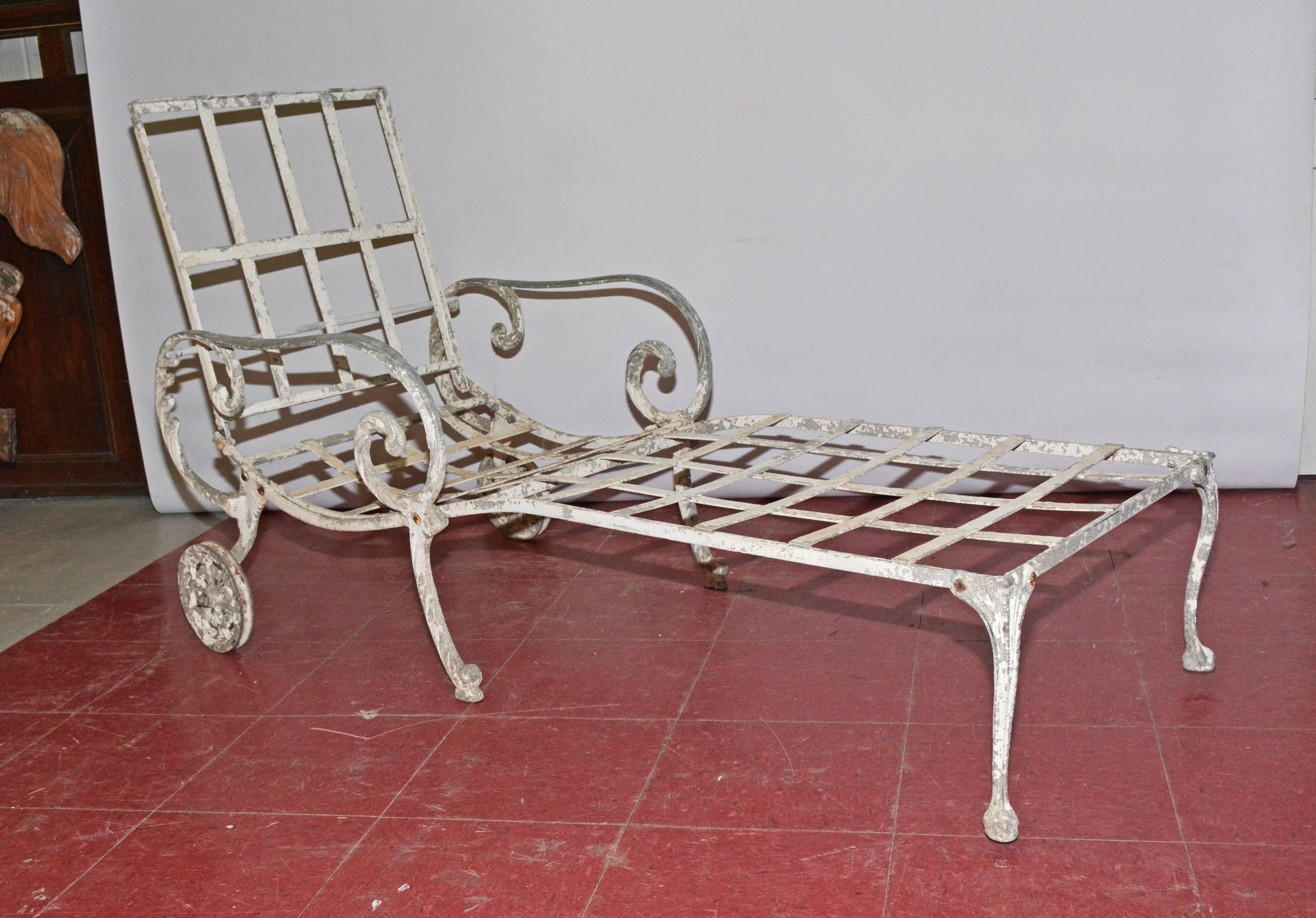 The vintage white wrought iron outdoor reclining chaise longue is moveable with its pair of wheels. The backrests on a moveable bar for flexible positioning or folds down for storage. The back and seat have criss-cross slats that will hold cushions