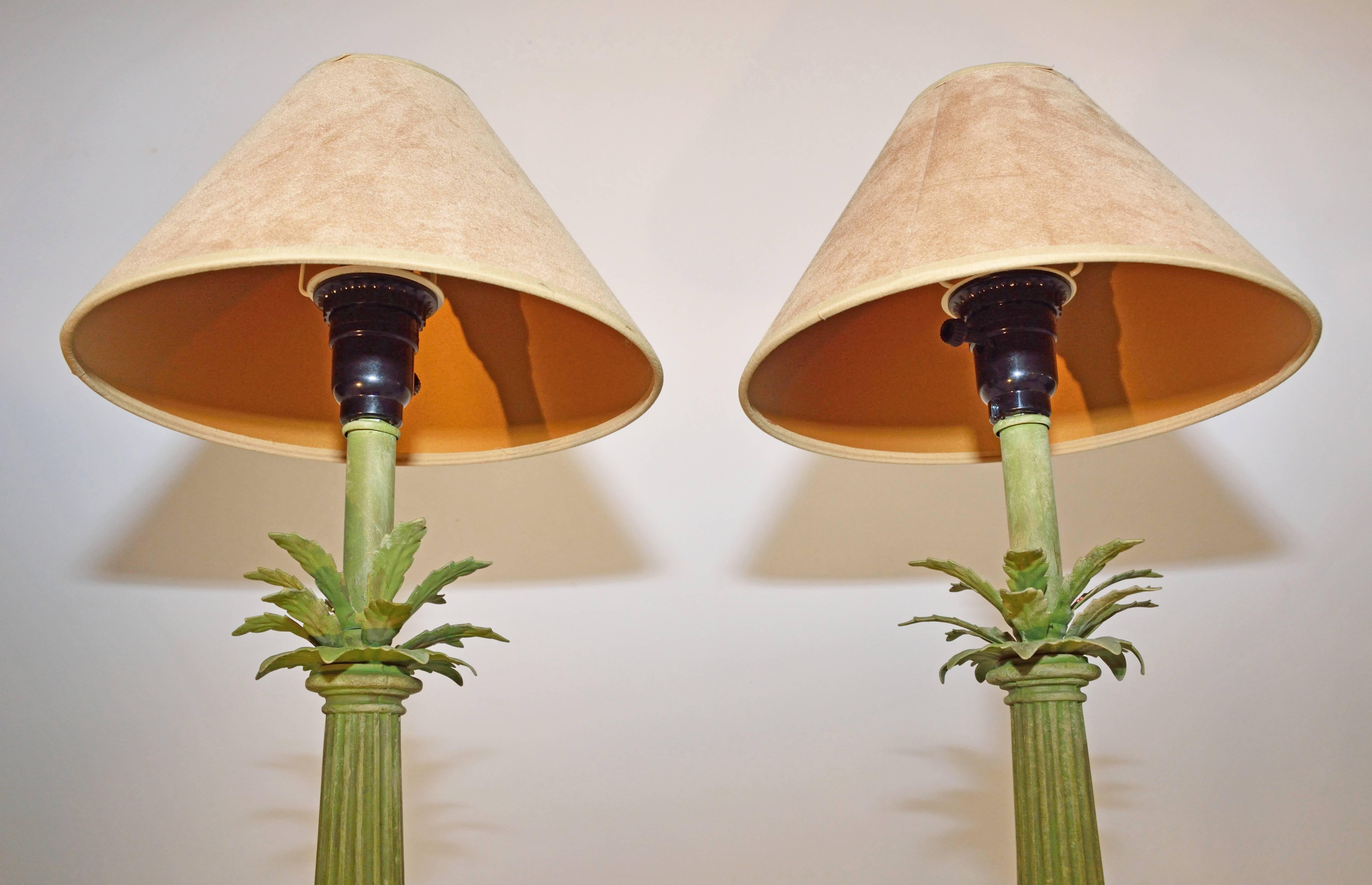 Pair of vintage lamps composed of tapered fluted columns set on bases and sprouting metal palm leaves at the top, all painted a mottled tropical green. The single lights are electrified for US use and have socket switches.

The suede-like tan