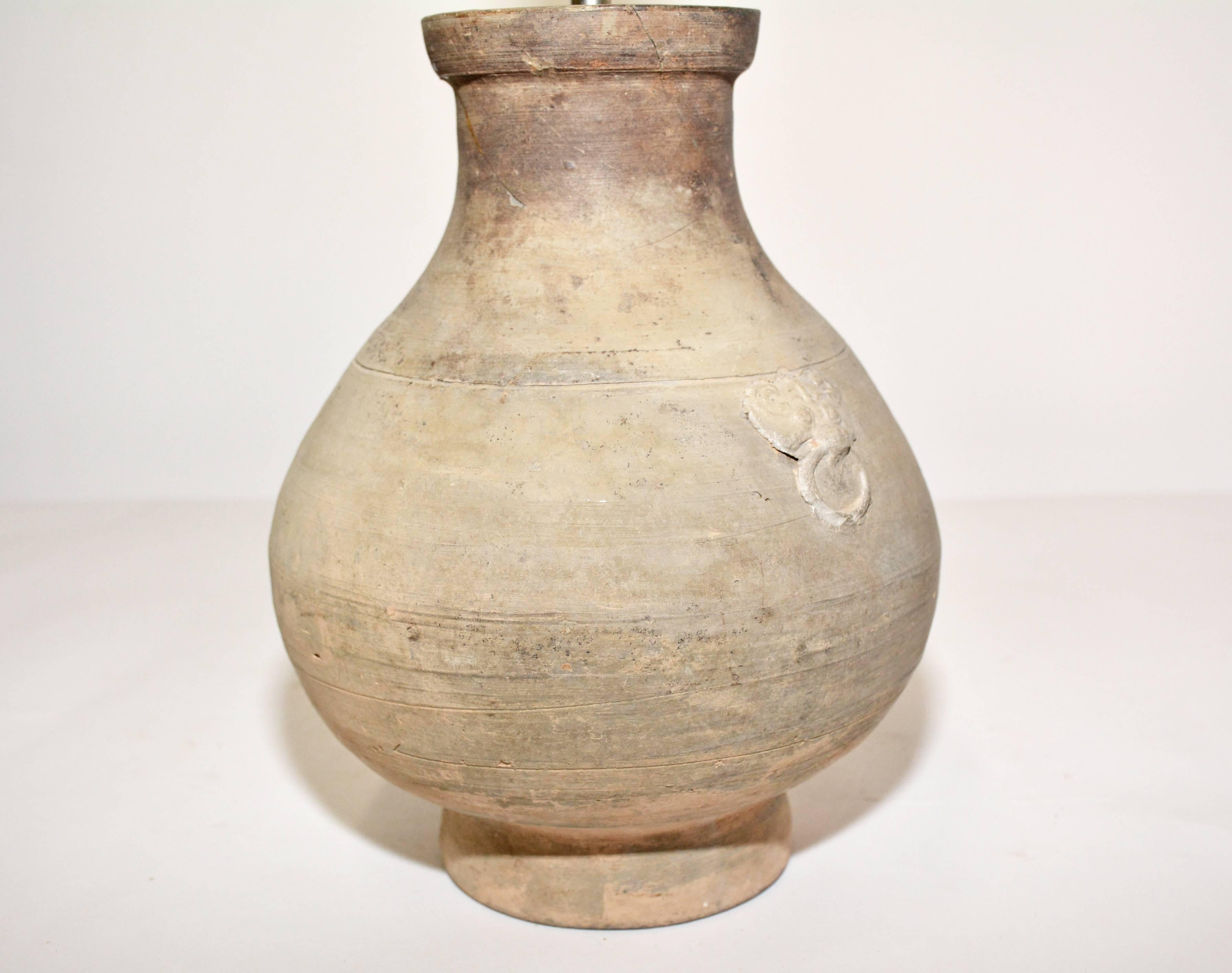 The lamp base is an antique unglazed pottery vase with a simulated ring on each side and residue of earth on lamp surface. The coolie shade is beige with an ecru plastic liner and a European mounting. The single socket is electrified for US use. 
