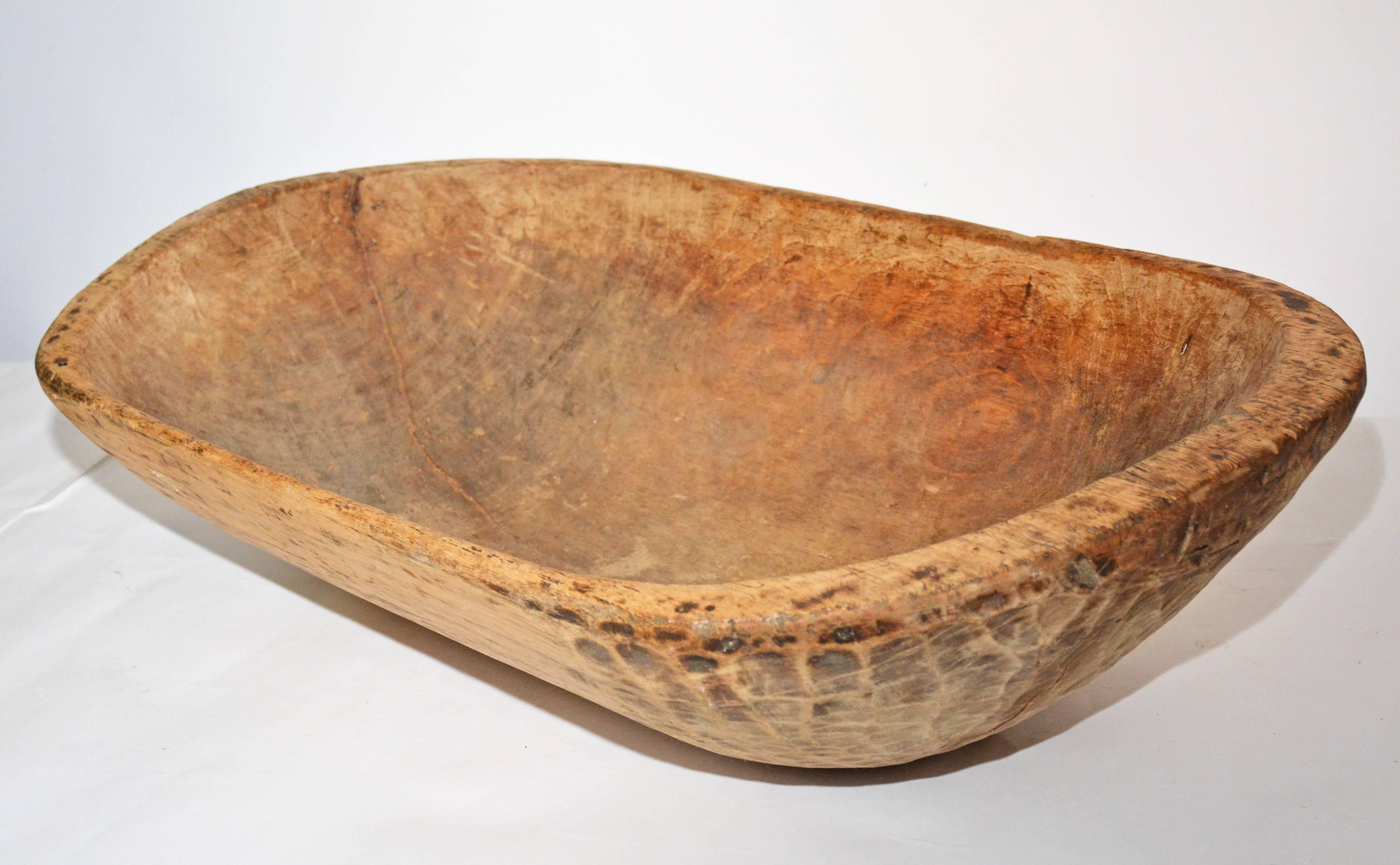 The antique elongated oval wood bowl is hand-carved and is made of a light-weight wood. The hand-carved markings can be seen. The bowl is thicker at the ends where there are handles than on the sides.