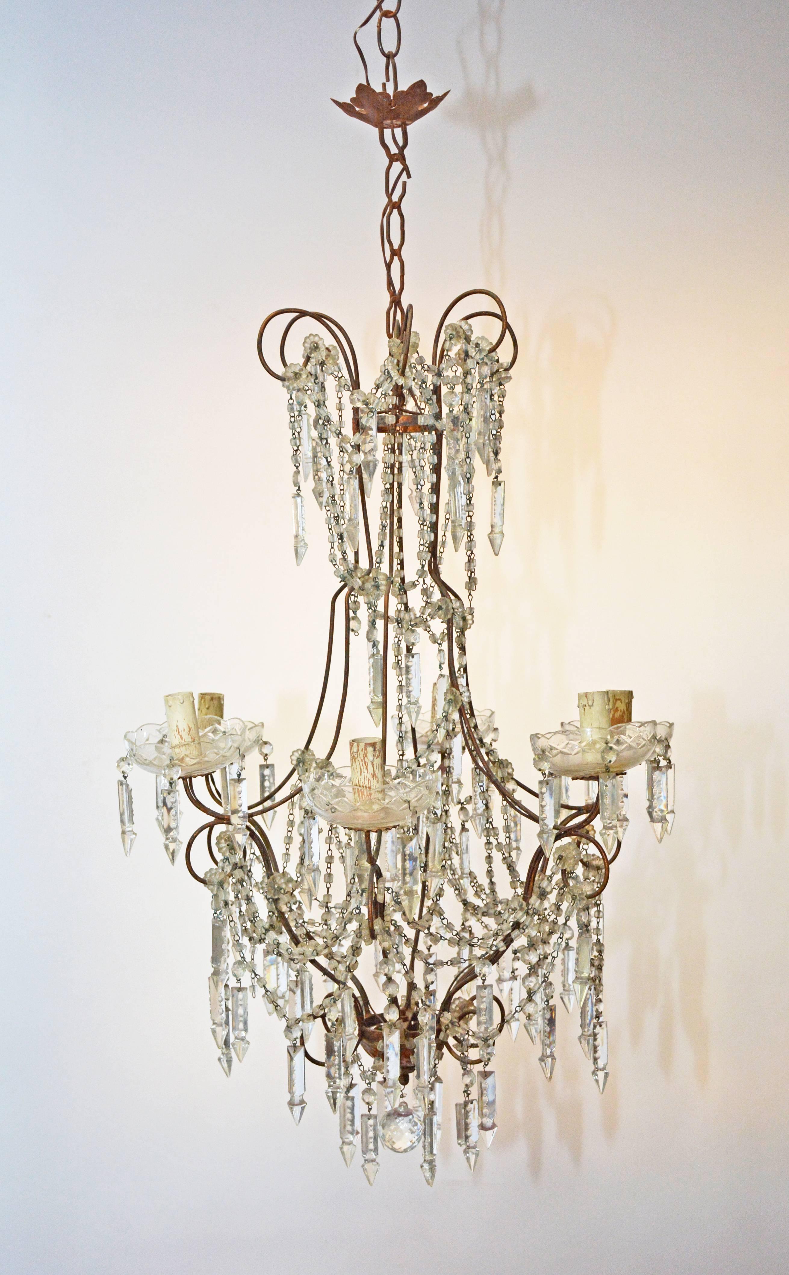 The classical vintage six-branch crystal chandelier is composed of a thin-tube frame from which hang icicle-type drops and overlapping ropes of crystals at two levels. Crystal bobeches support the light fixtures which take flame bulbs. The