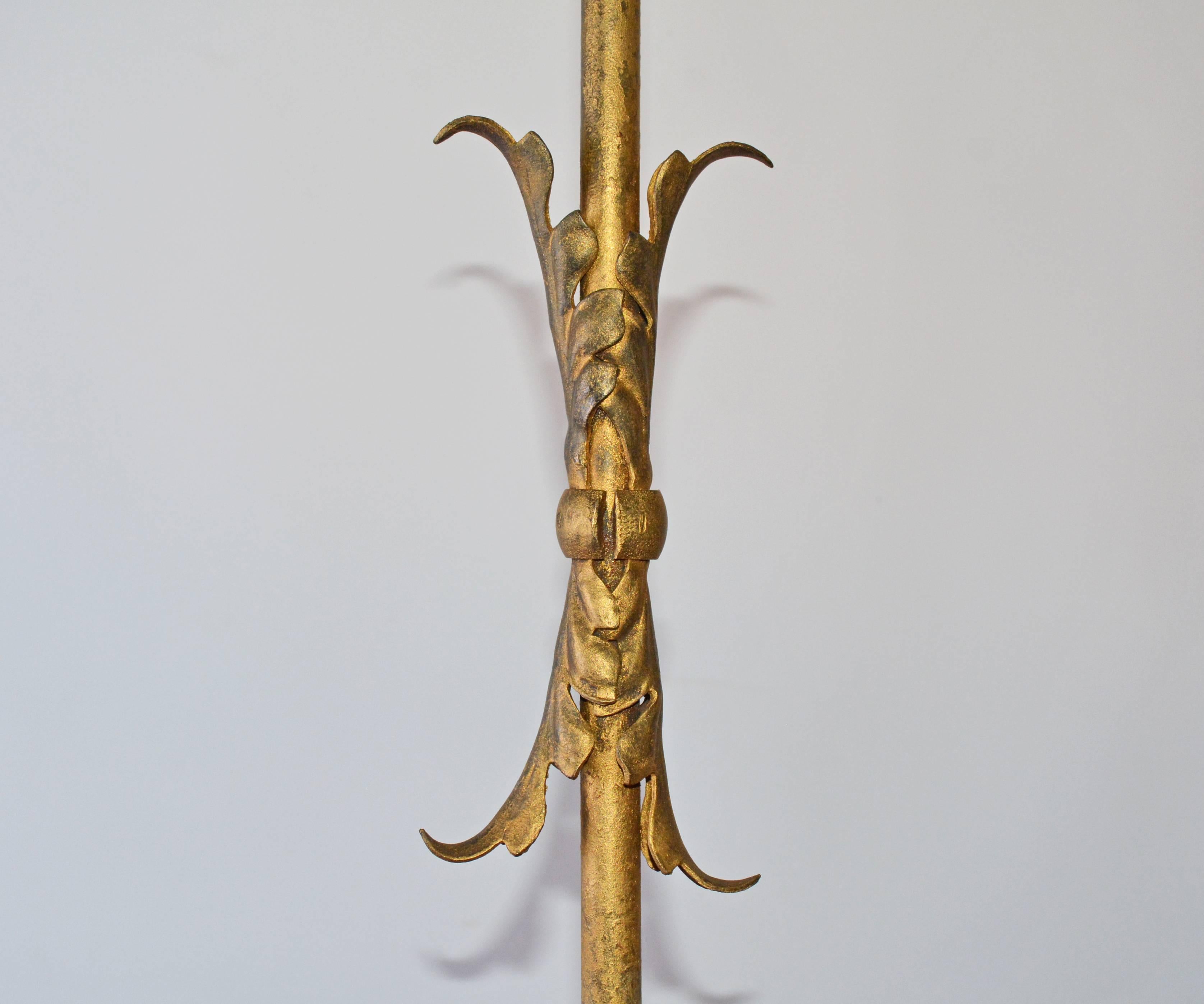 Le lampadaire en métal doré a trois pieds évasés et un mât central décoré de feuilles appliquées en métal doré. La lampe est électrifiée pour une utilisation aux États-Unis avec deux luminaires dotés chacun d'une chaîne de traction. L'abat-jour en