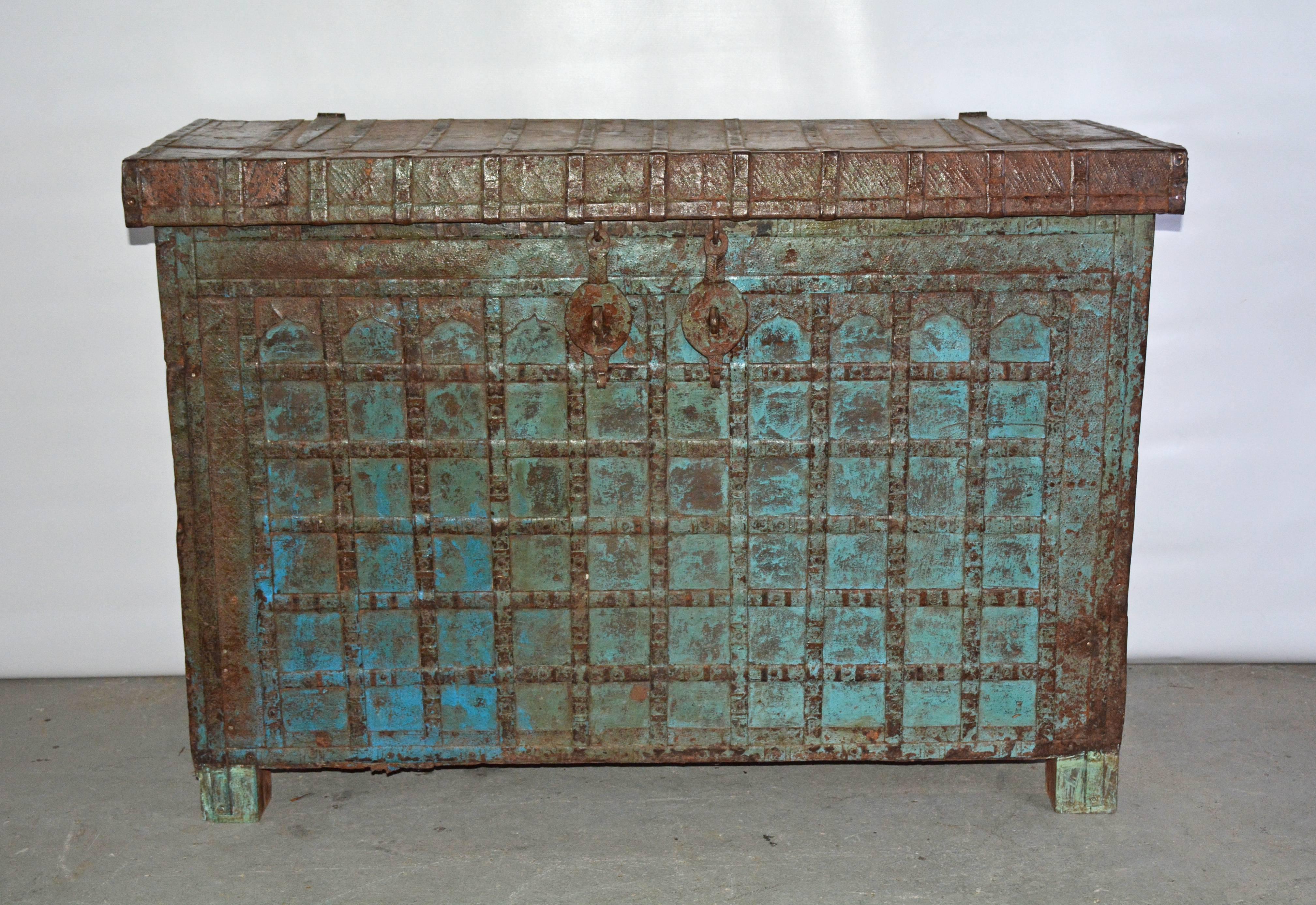 Great statement piece, this tall antique Indian chest or console table is painted blue and has crisscrossed iron strapping secured to wood. Embossed iron panels frame the top and front. Wood legs. Pairs of iron hinges, latches, side handles and a