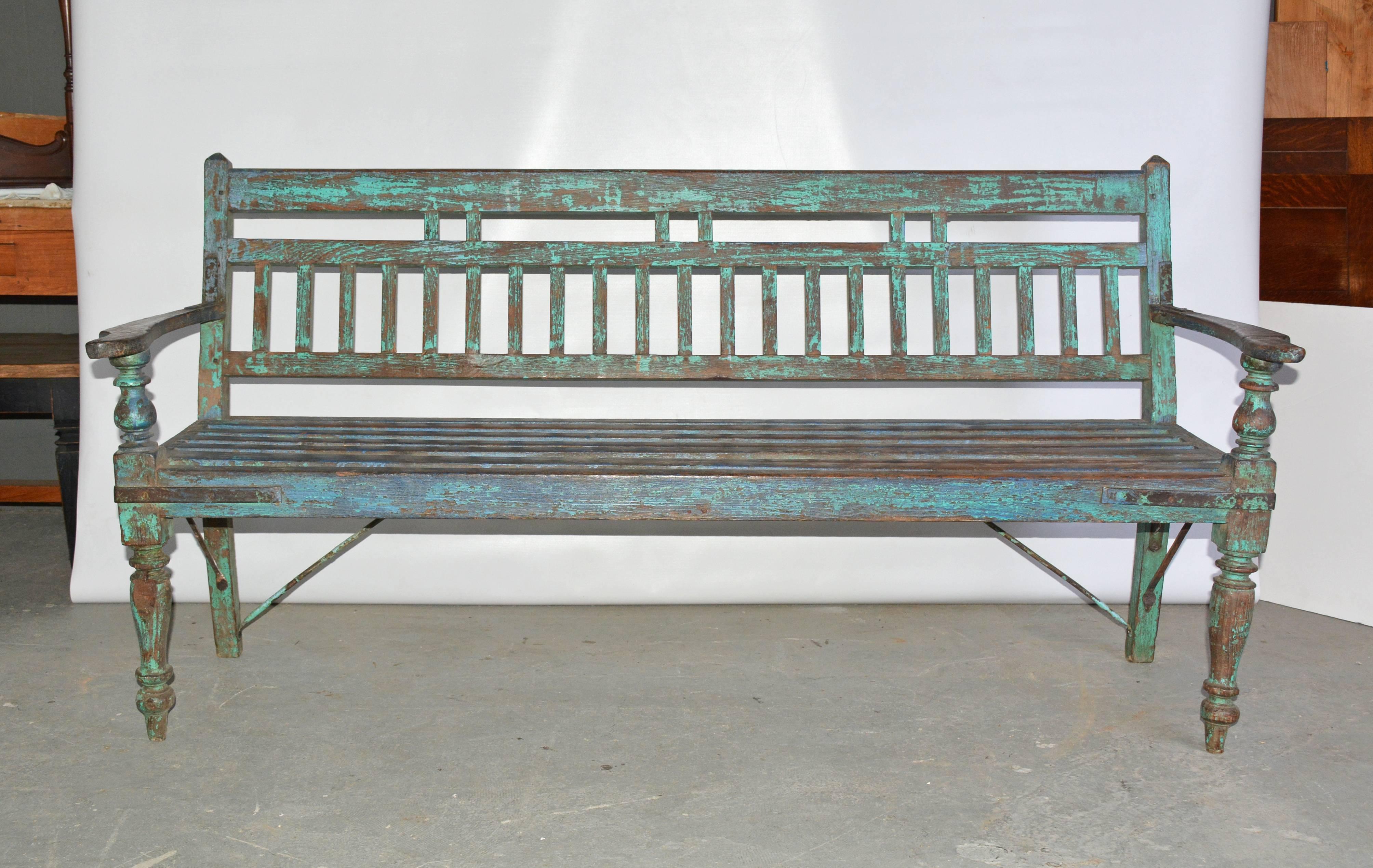 The Dutch colonial garden/porch teakwood bench with painted blue-green wood has turned front legs and arm supports, metal rod supports and metal braces. The slatted seat is slightly concave.

Measures: Arm height 24.88".