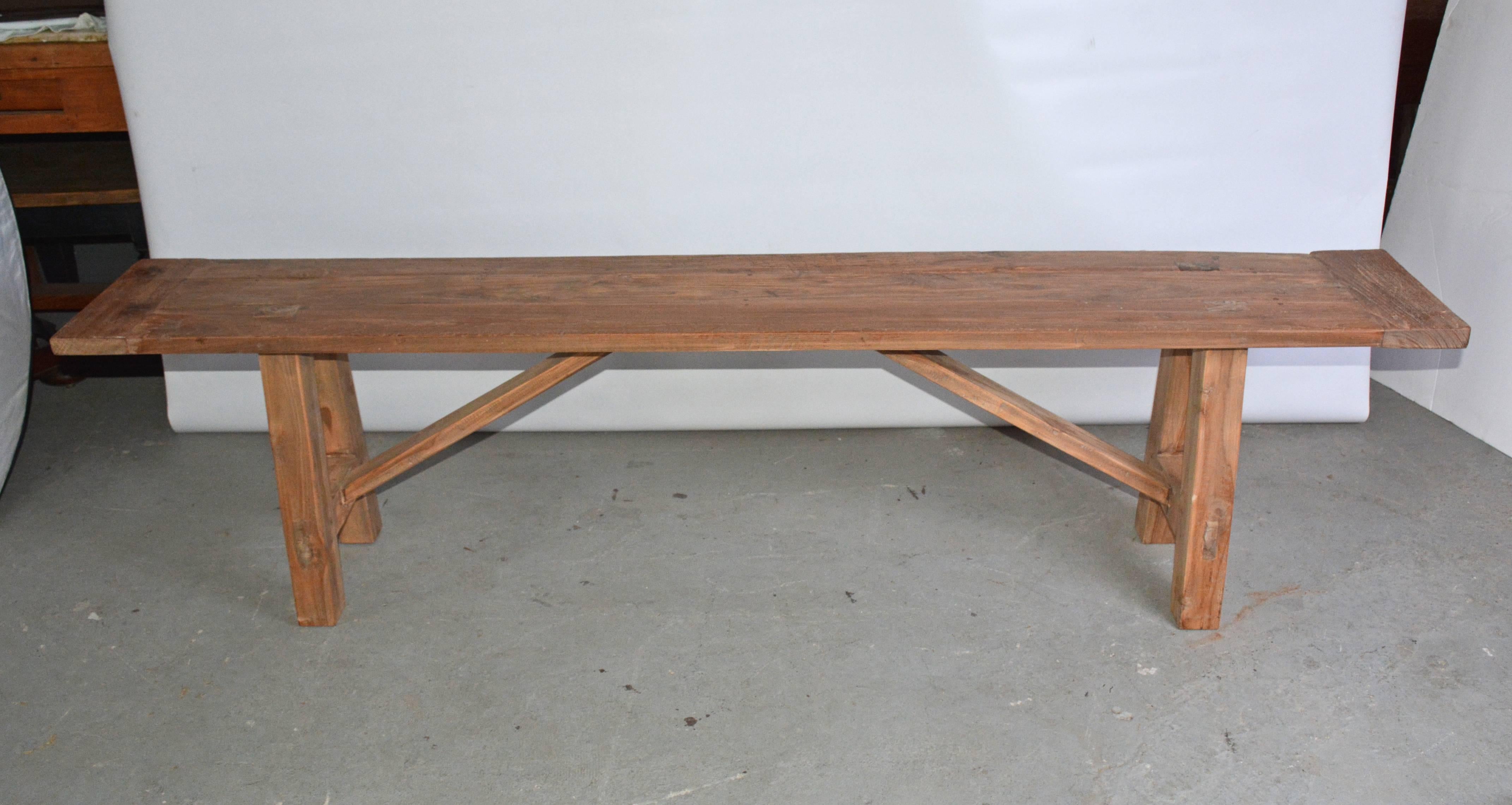 The rustic teak bench has splayed legs pegged into the breadboard top, stretchers and angled supports. Great as garden or porch dining seating.
