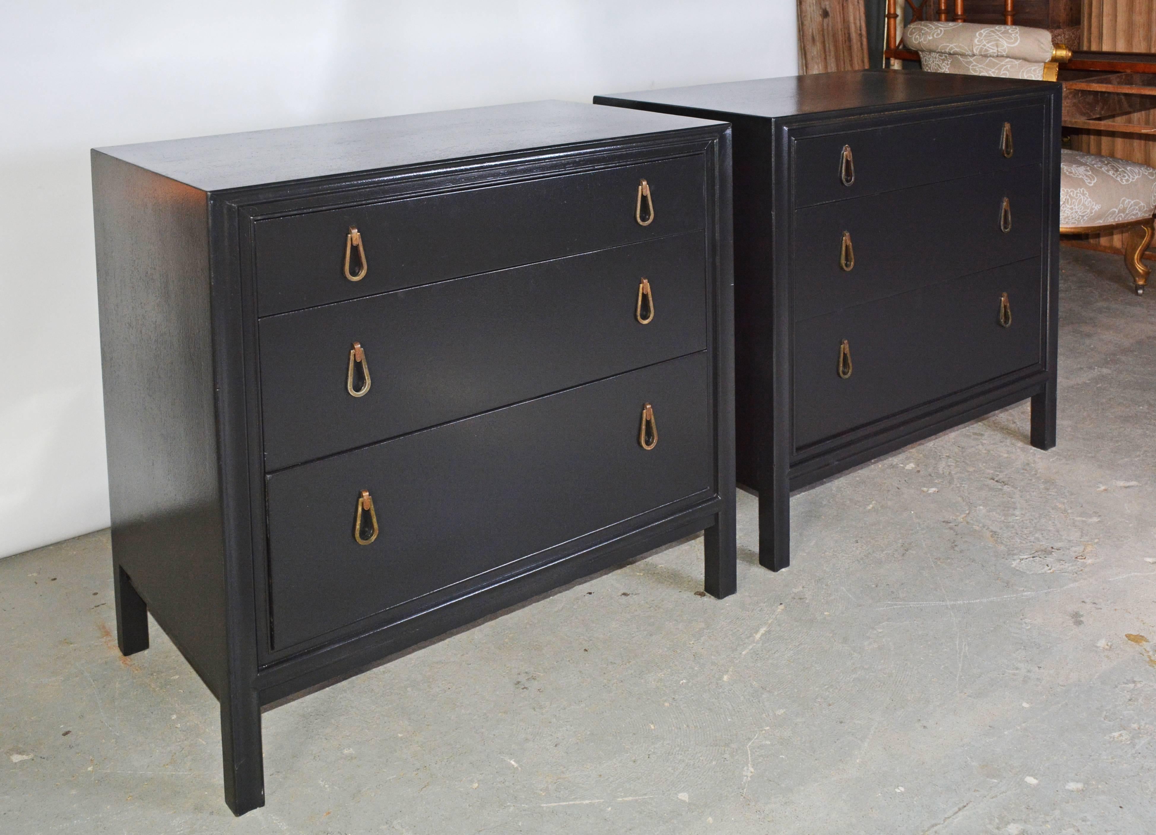 The pair of wood Moderne chests are painted black. Each has three dovetail drawers of varying heights and inset brass loop pulls. Can be used as nightstands or dresser.