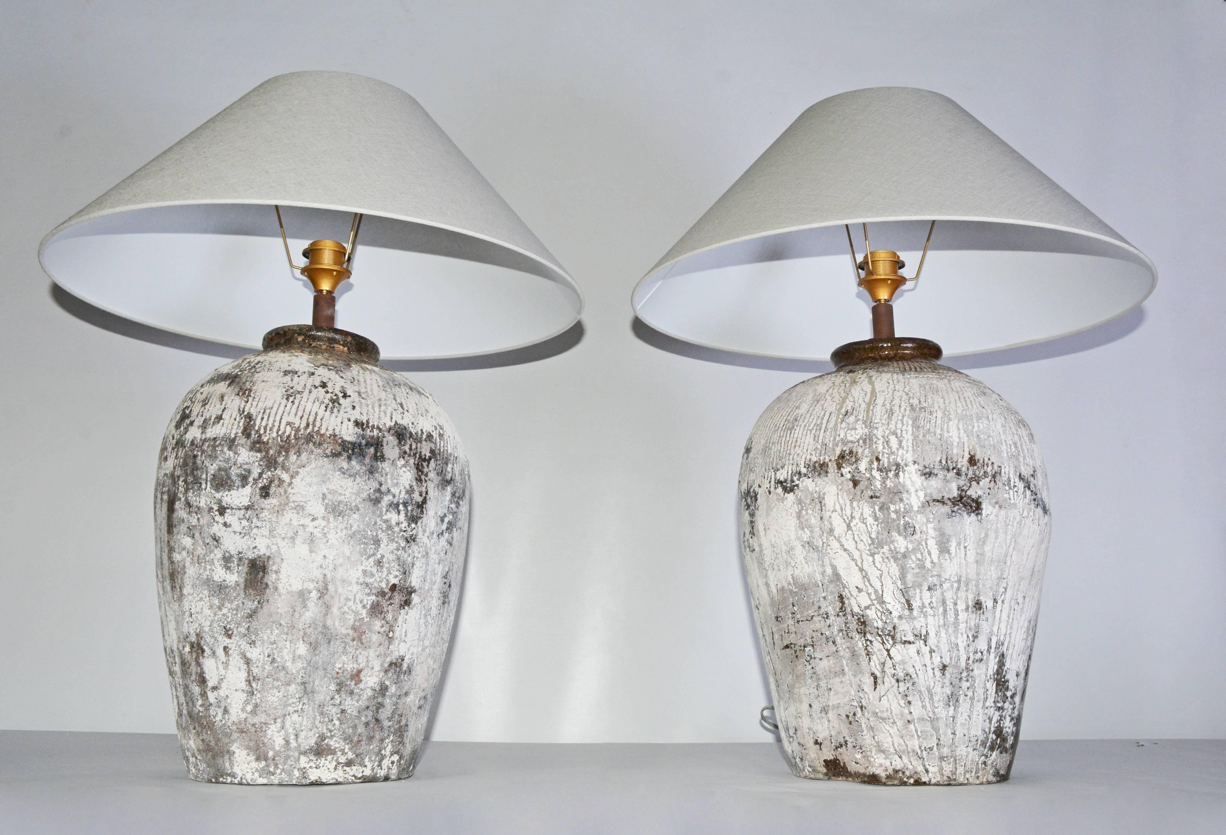 Almost a matching pair of large table lamps made from rustic vintage Chinese clay wine storage jars with a black and white mottled pattern and ribbed surfaces around the tops. The shades are made of pale grey cross-hatch linen. 

Shade height: