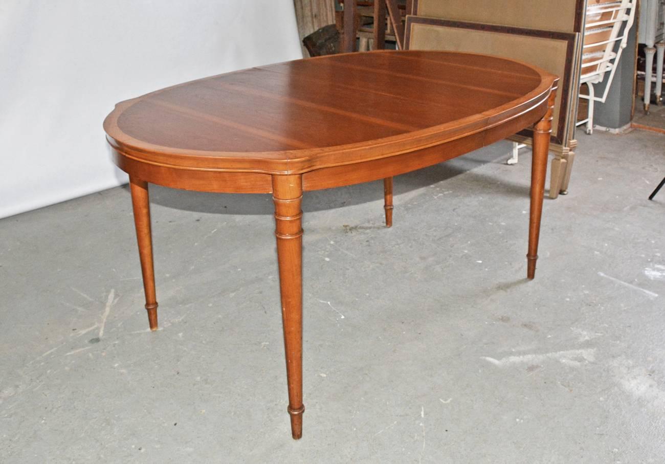 The vintage oval dining table has two types of wood with the lighter wood as a frame for the darker center. There are two ends and two leaves, all of which are supported by two expandable iron braces underneath. The legs a round and tapered. The