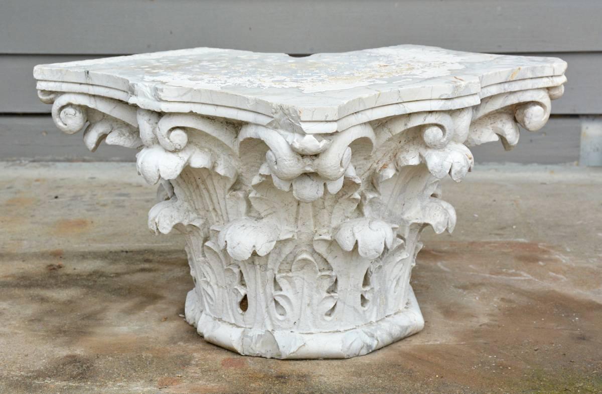 The antique Corinthian corner capital is made of veined marble painted white. One corner is cut away so that the capital can protrudes from the corner of a building. Two layers of acanthus leaves support scrolls sitting under the top platform. Can