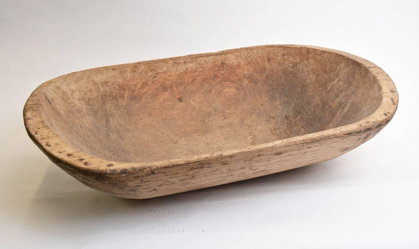 The large extended oval rustic wooden bowl is hand-carved with chisel marks on the underside. A pair of shallow handles are also hand-carved. The bowl maintains its natural finish. Great as centre piece for a harvest table.