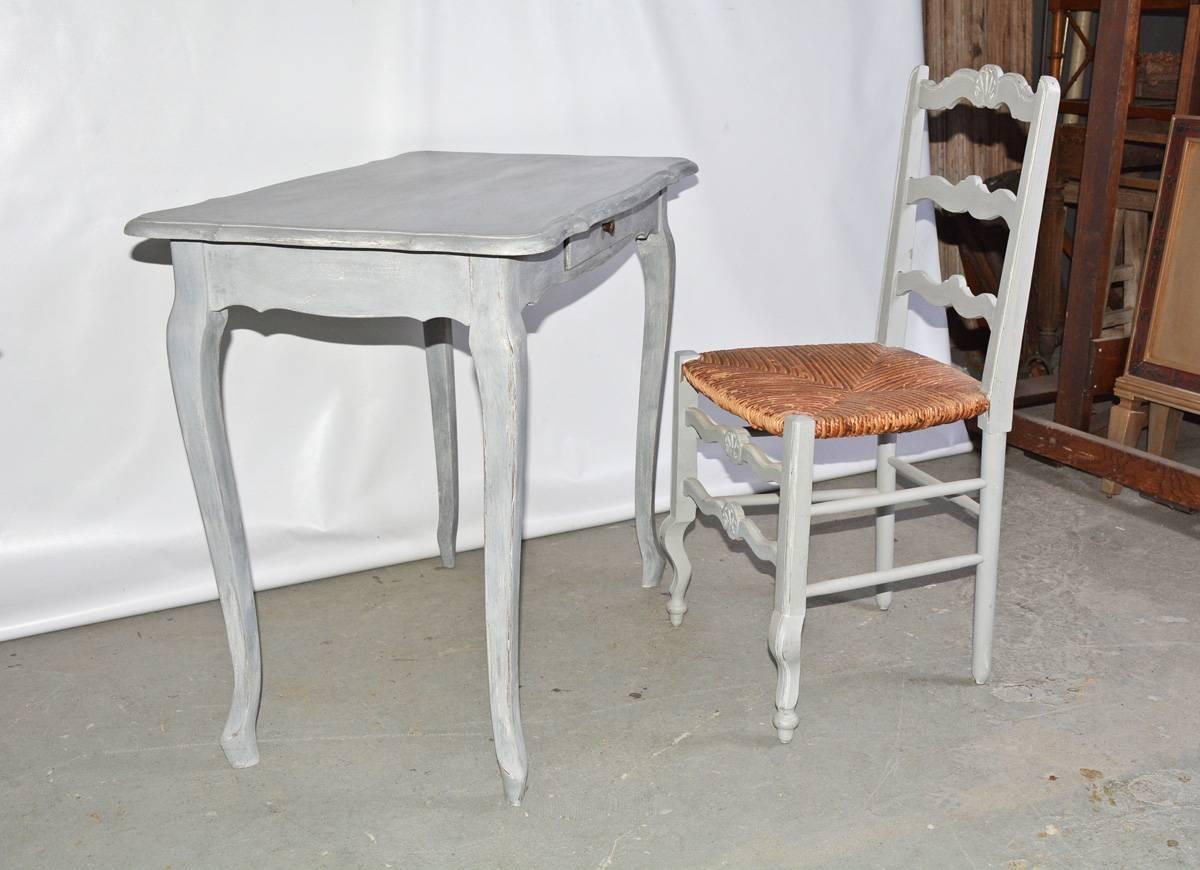 The desk and chair are vintage country French in the Louis XV Provincial style. The table is perfect as a dressing or lamp table or small writing desk. Has a single drawer with brass pull. The ladder back chair has a raffia seat. Both are painted