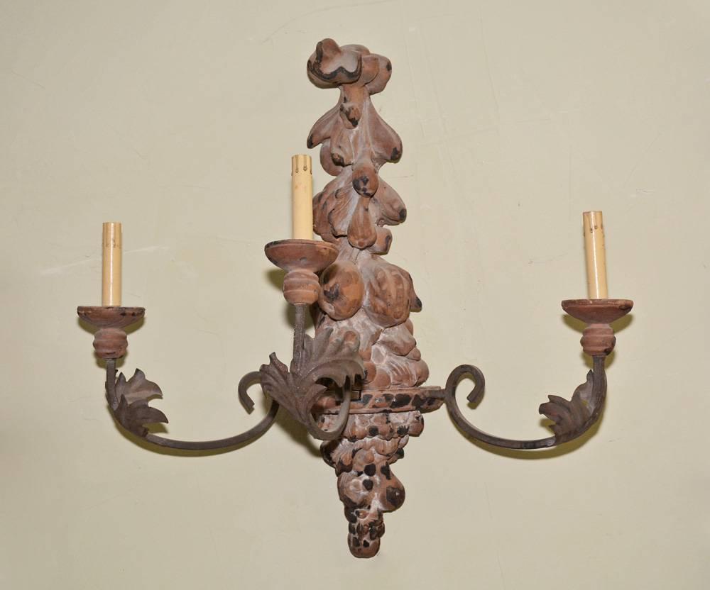 Cette applique ancienne en bois peint et sculpté à la main, de style baroque, comporte trois armatures en fer forgé câblées électriquement pour des ampoules à flamme américaine. Le motif est une superposition de fruits et le bois est peint en brun.