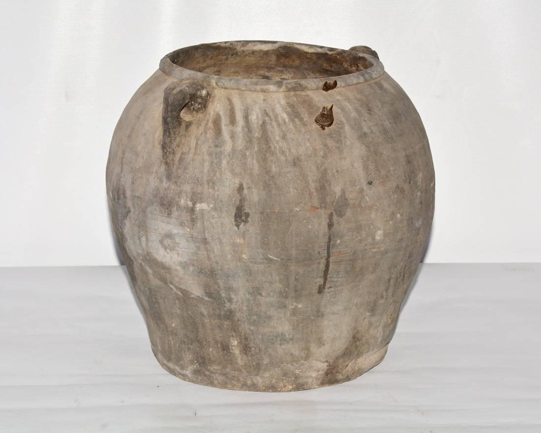 The Chinese clay jar is handcrafted and has two small handles. Shallow en relief bands encircle the upper part of the vessel. The organic rich dark clay is from a Chinese river basin.