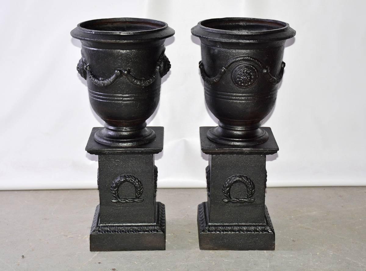 The pair of vintage anduze style vase or planter with pedestals made of cast iron. The urns are decorated with swags and have holes in the bottoms for drainage. The pedestals are open at the top and are hollow. They are decorated with wreaths.

Urn: