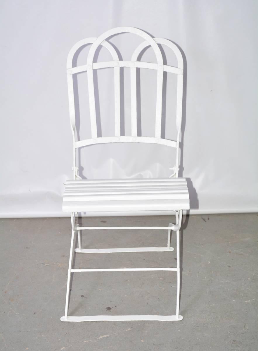 The antique French bistro chair folds flat, is made of painted iron with a decoratively curved back and has wood slats for seating. Newly painted white.