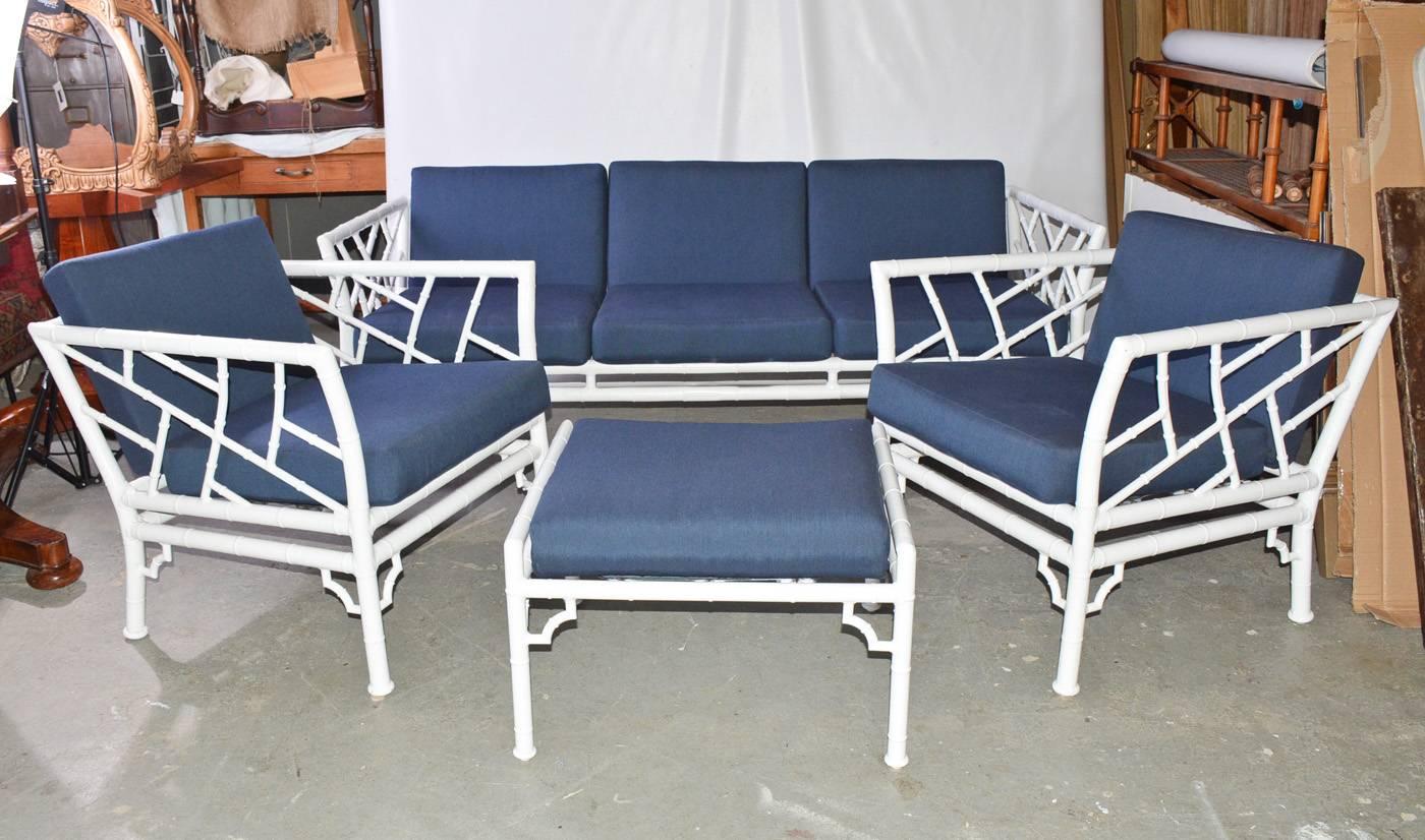 The four-piece indoor or outdoor vintage faux bamboo patio, garden or porch set has two armchairs, a three-seat sofa and a stool. The pieces are made of metal painted white. The cushions are upholstered with a blue zippered fabric. Under the seat