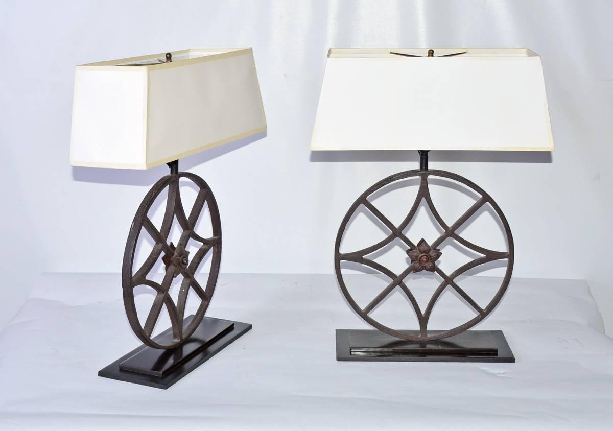 The pair of black wrought iron lamps are circular architectural elements fitted with centered rosettes. The elements sit on stepped bases of polished iron. Electrically wired for US use. The rectangular shades are made of white translucent plastic.