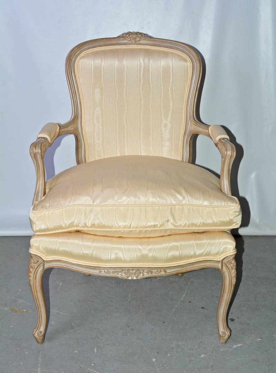 The vintage Louis XV-style bergere arm chair is upholstered in a cream moire fabric and has a down feather cushion. The hand-carved light wood frame is lightly white washed. 

Measures: Arm height 25.75