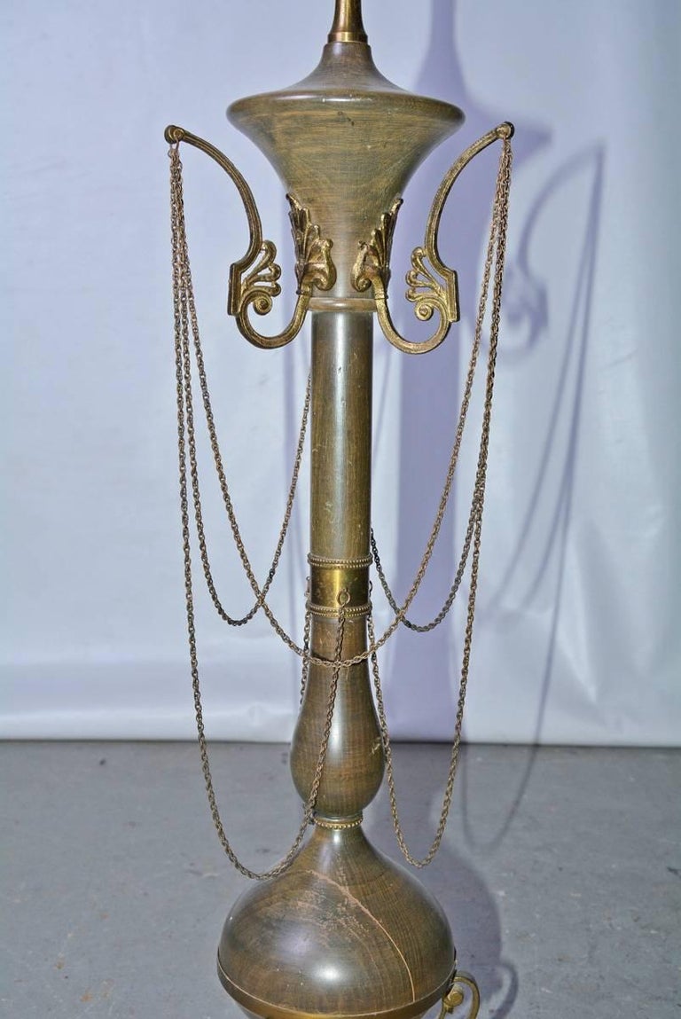 The antique table lamp in wood with gilt metal embellishments is designed to resemble an ancient torchere. Six looped chains and stylized acanthus leaves denote the ancient motifs. The wood is painted while gilt metal curved feet are attached to a