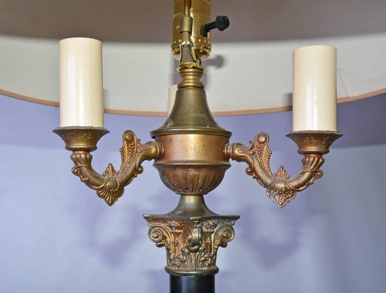 The black painted and gilt metal neoclassical floor lamp has elements of a classical column with a Corinthian capital and secondary base. In between is a black shaft. All rests on a wide circular black and gilt metal base. The shade is made of cream