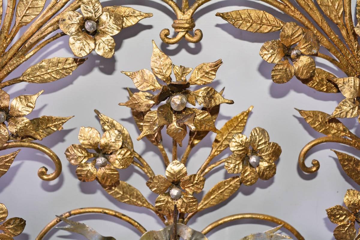 The elaborate Italian gilt metal floral wall decoration has spikes located up the sides and at the top and bottom for holding 14 candles. The whole composition is held in place with a silver gilt, rippling metal bow. The centers of the flowers are
