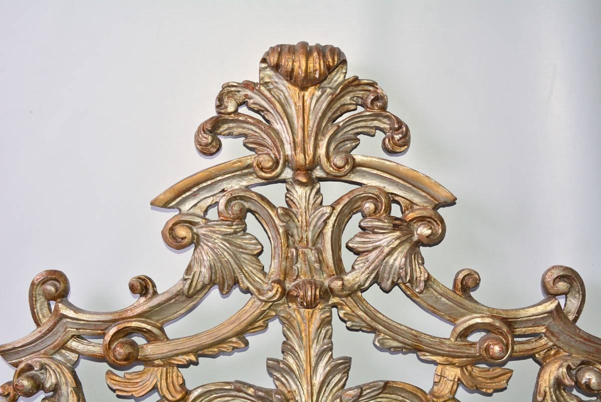 The antique hand-carved wood ornament is painted in silver gilt. The decorative elements are attached to a horizontal board at the bottom that has rectangular slots underneath, two in the middle and one at each end. In the back is a vertical flat