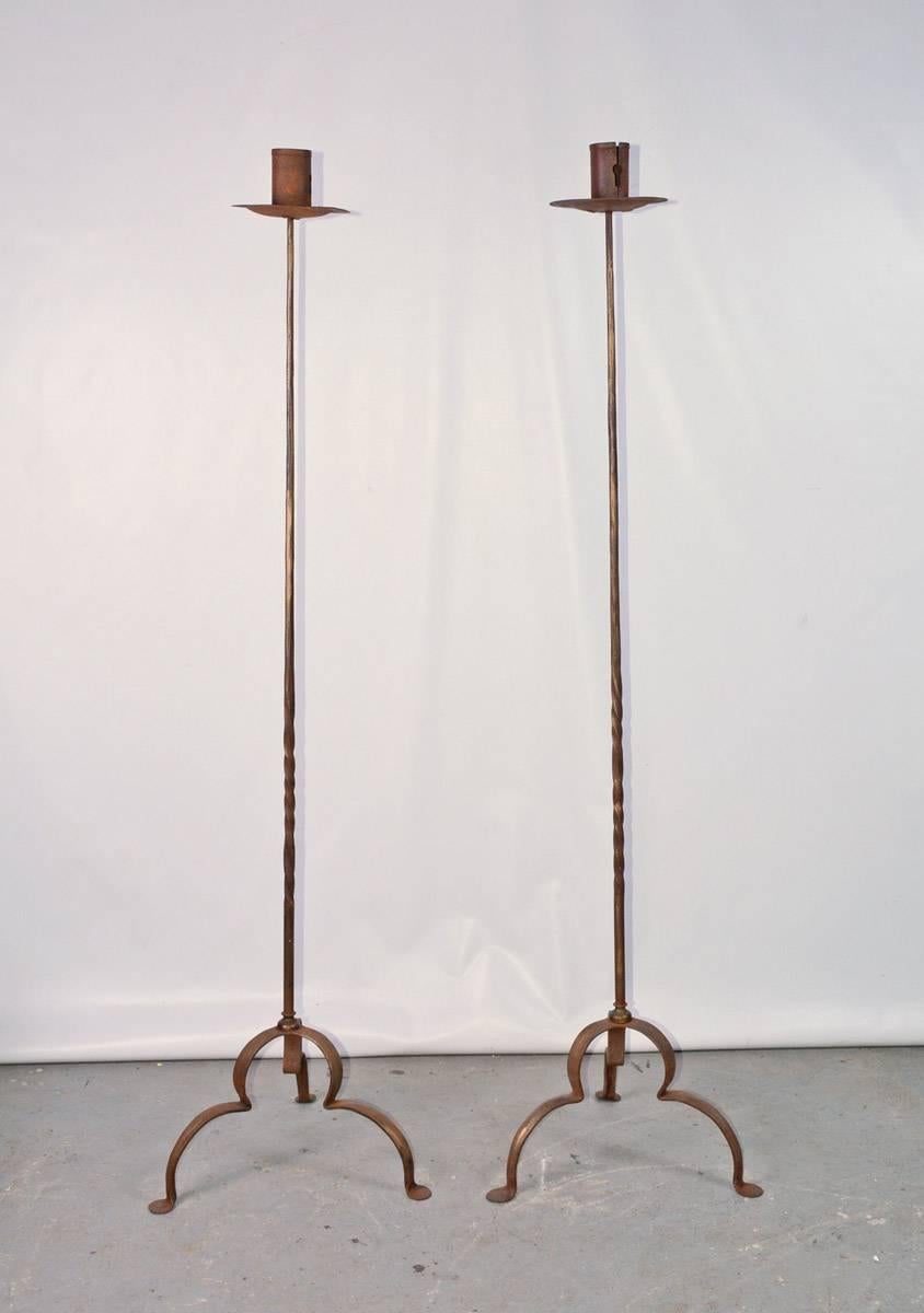 Rustic and elegant, each of the pair of stylish antique gilt handcrafted wrought iron tall stand candleholders or floor torchières has three curved legs, partially twisted decorative shafts and bobeches. The candle holder have 2