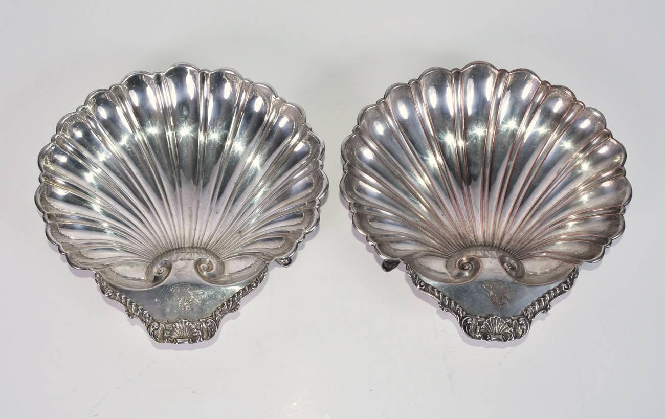 The pair of 19th century British silver-on-copper footed serving dishes are in the shape scallop shells. The handles are topped with scallop shells as well and have engraved British coat-of-arms in the shape of the rampant lion and crown. The