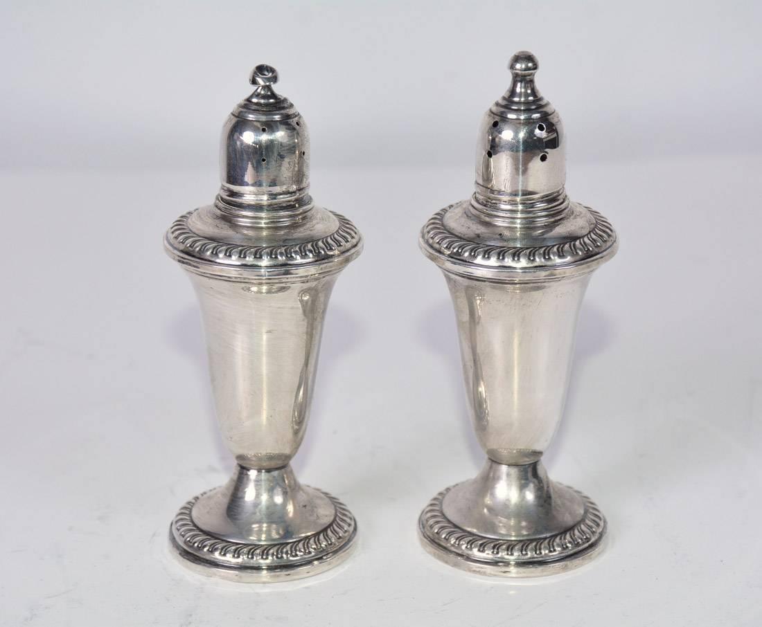 The mid-20th century sterling salt and pepper shakers have glass liners to avoid corrosion. The tops and bottoms of the bases are embellished with a classical gadrooning design. Stamped on the bottom 