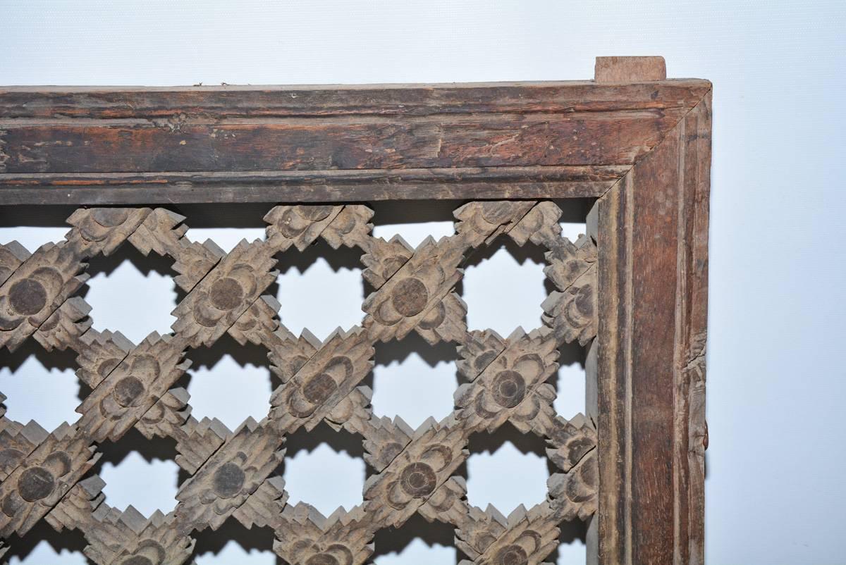The antique window screen is made of hand carved wood. The pieces of the diagonal stepped design are slotted and fitted where they cross. The frame is grooved and has pairs of rectangular pegs top and bottom for securing the piece to a window