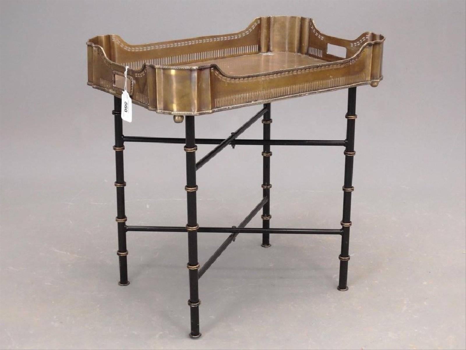 The vintage brass gallery tray coffee table or side table sits on crisscross table legs that collapse for easy storage. The tray has filigree sides and the metal legs are painted lacquer black with spaced gold rings imitating faux bamboo. The top of