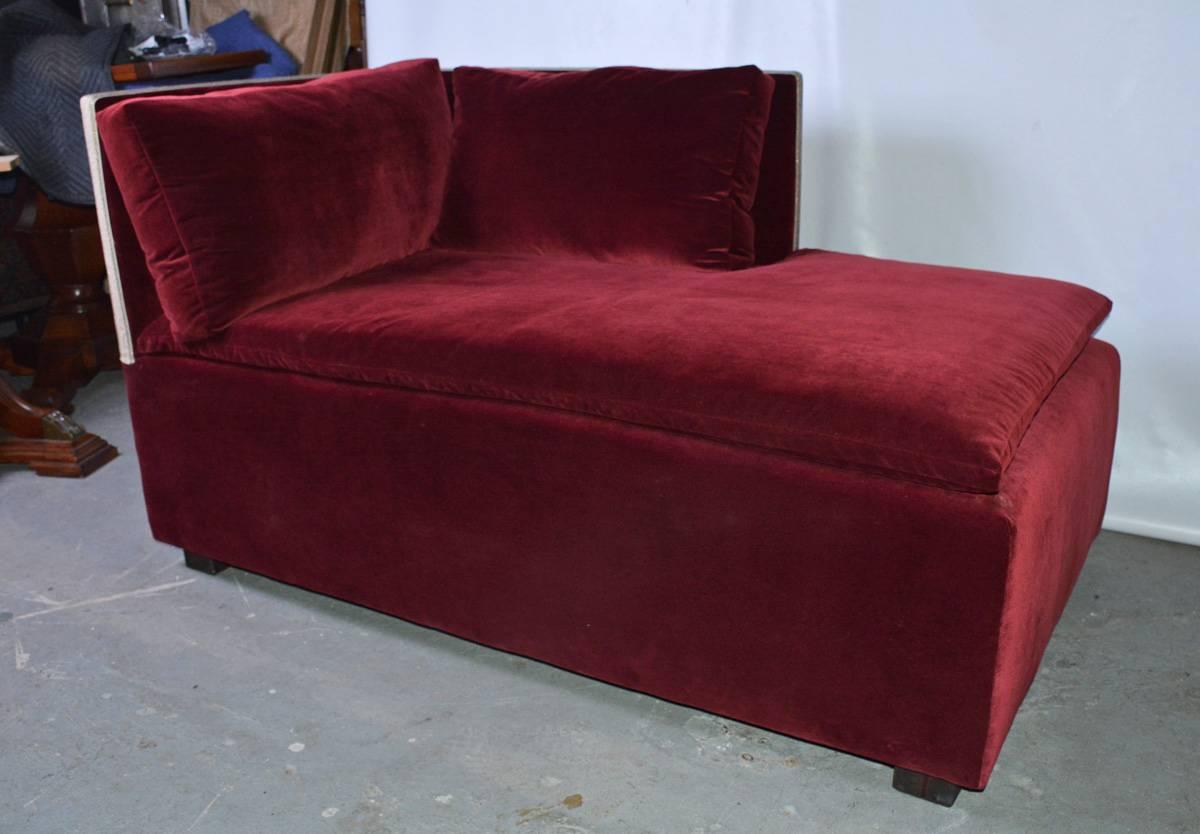 The custom made contemporary chaise lounge in the style of Juan Pablo Molyneux with an open side is upholstered with burgundy colored cotton velvet fabric and edged with a white and silver woven ribbon. The back and side cushions are down and the