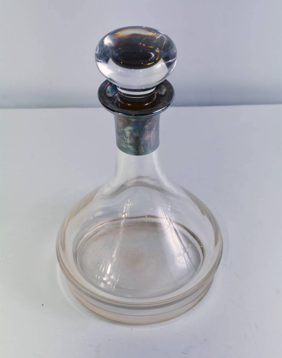 The contemporary crystal wine decanter, with a pale amber cast, has a silver overlay collar and a crystal stopper. Because of its wide bottom, the nontipping piece is called a 