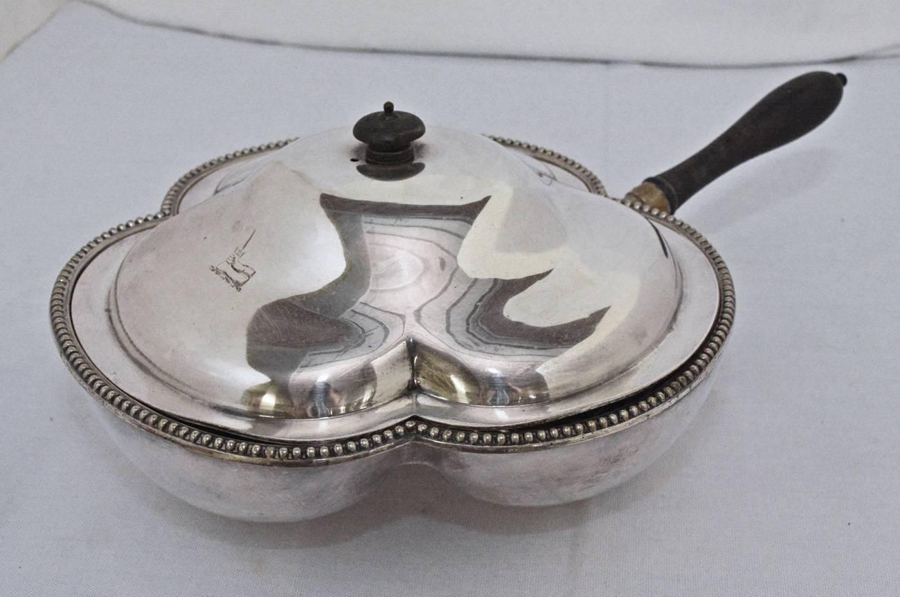 The late 19th century silver plated dish with lid is English and has three cavities for serving different foods and a space below for hot water. The handle and knob are teak. The lid fits within the beaded edge. The bottom of each section has a