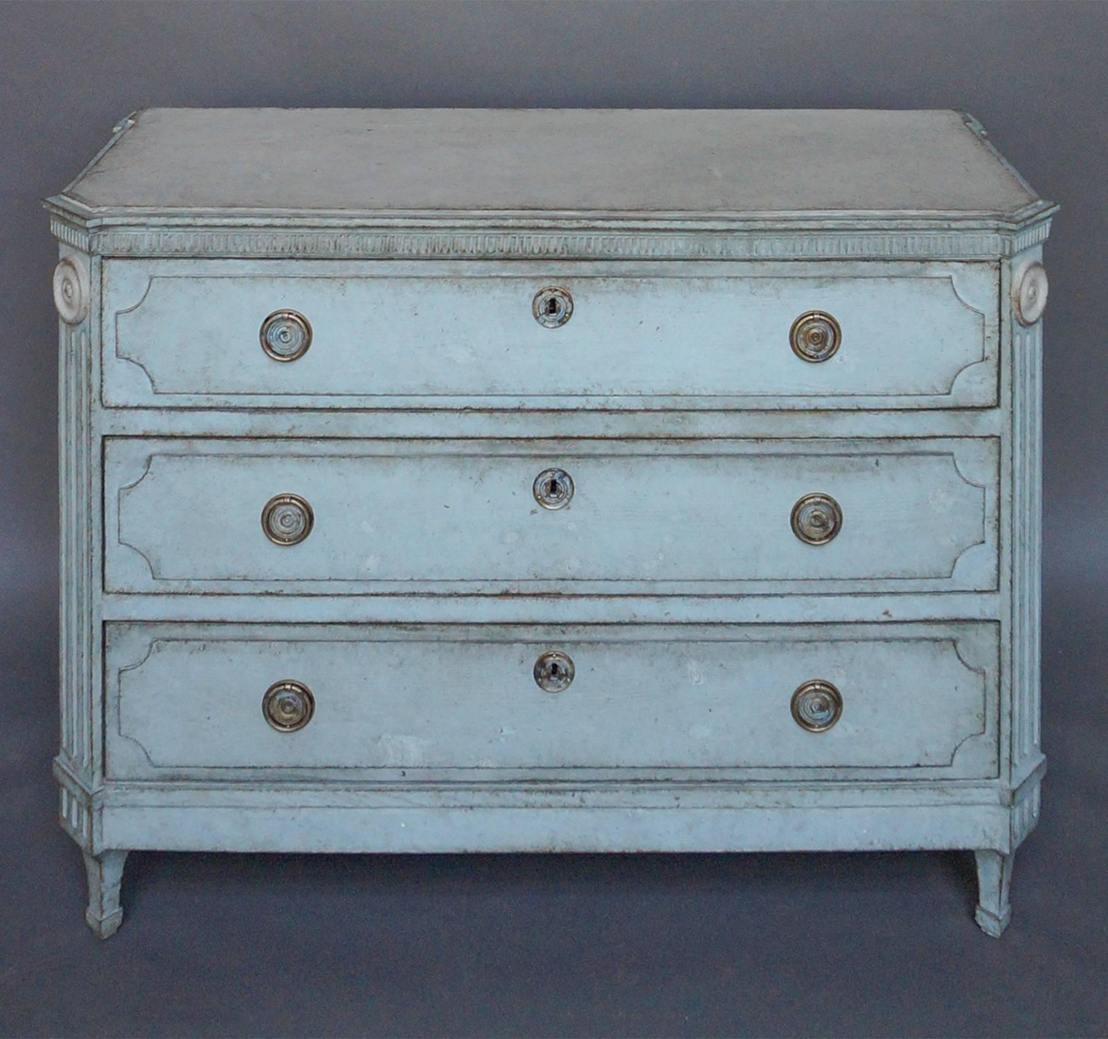 Chest of three drawers, Sweden, circa 1840, in pale blue paint and with a reeded panel under the shaped top, canted corner posts with fluting and raised panels on each drawer front. Brass pulls and escutcheons.