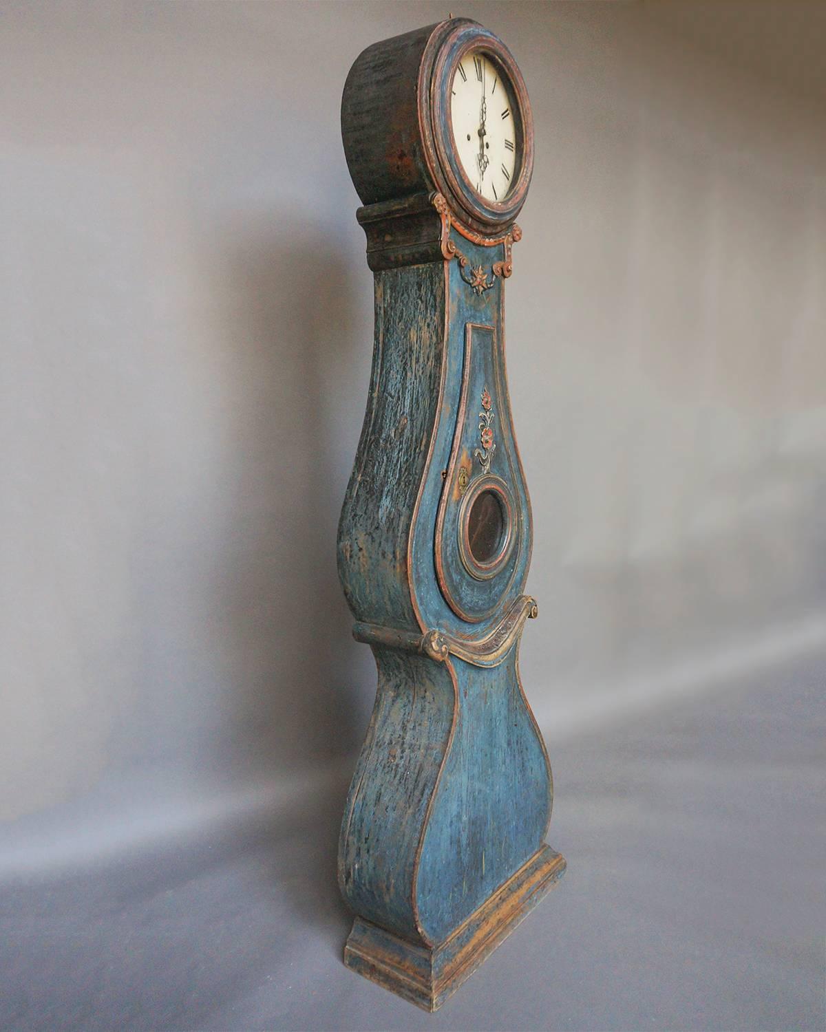 Beautifully carved and painted tall case clock from Fryksdalen, Värmland, Sweden. Just below the face is carved detail reminiscent of a garland of flowers. Roses decorate the middle of the case and below the “belly” of the clock is a carved band
