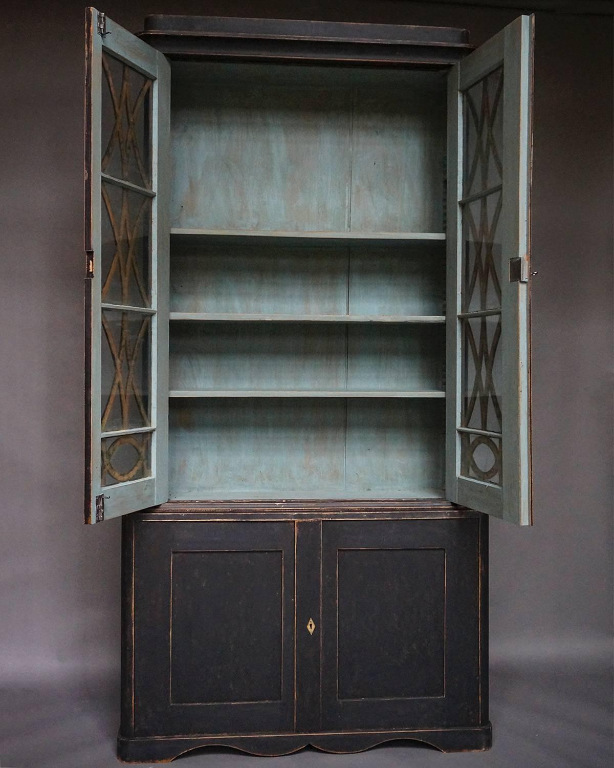 Two-part bookcase and cabinet in black paint, Sweden, circa 1830. The top section has four shelves behind double doors with the original glass. The lower section has a single shelf behind double doors, all on a shaped bracket base.