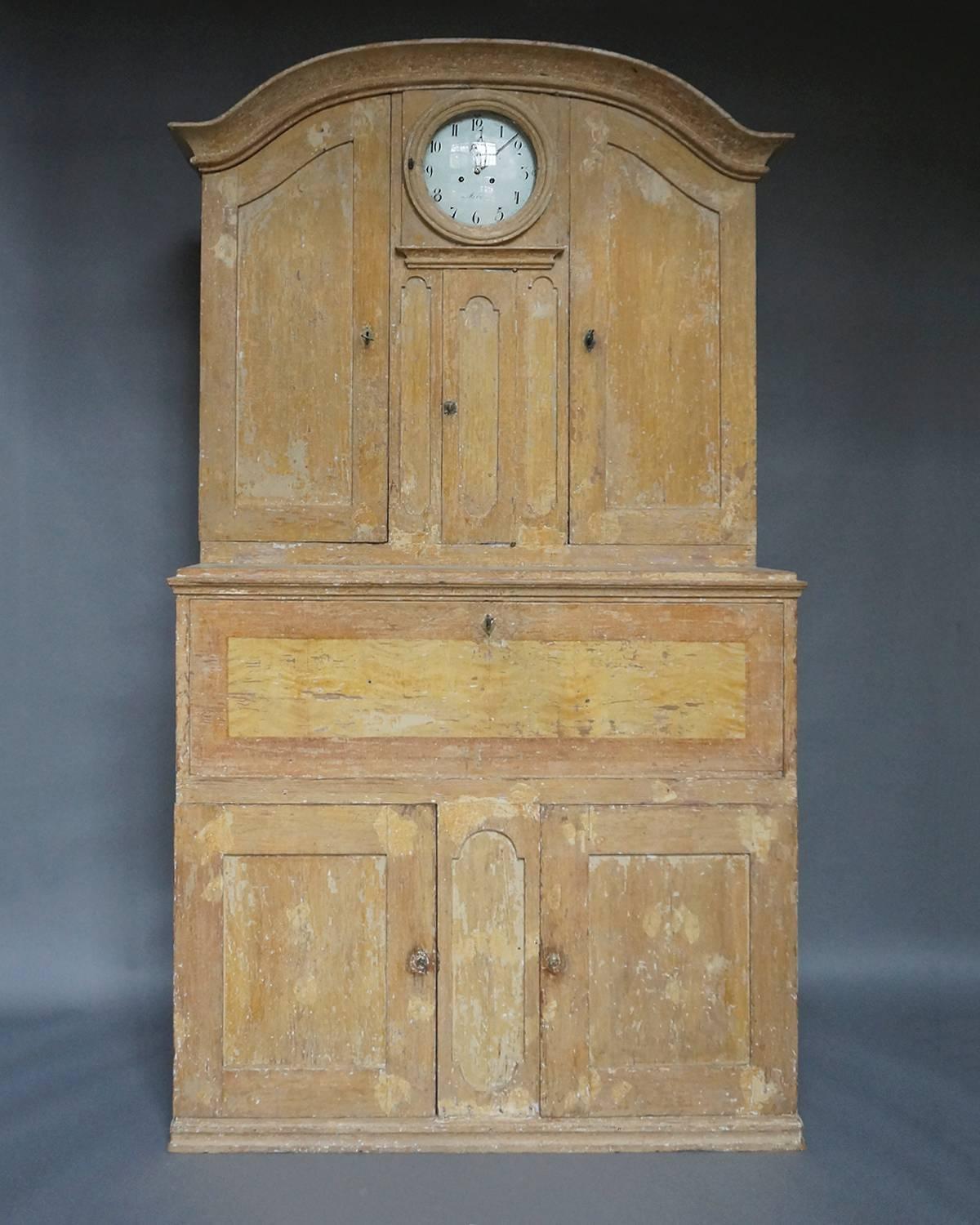 Period secretary from Hälsingland with integral Mora clock and with original paint, Sweden, circa 1840. On either side of the clock is a cabinet with arched doors and three interior shelves. Behind the fall front are two banks of three drawers