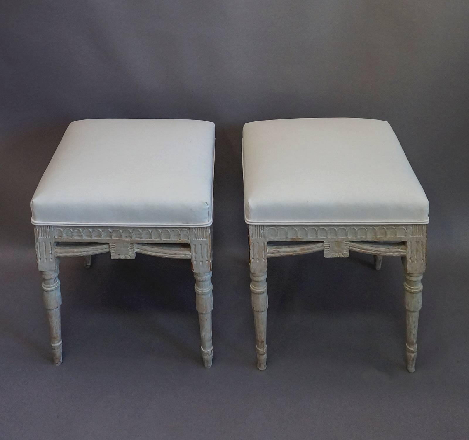 Pair of square stools with carved frames, Sweden, circa 1900. Lambs tongue molding around the upholstered seats and swags between the turned legs.