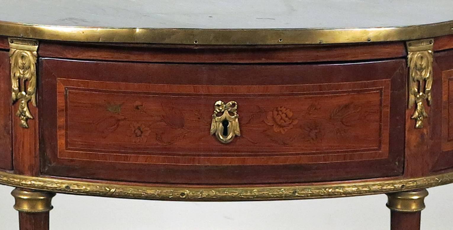 A Louis XVI gilt bronze mounted
tulipwood marquetry console desserte,
last quarter of the 18th century.

The D-shaped gray marble top with three-quarter pierced gallery, above a frieze drawer inlaid with vines of flowers flanked by hinged doors,